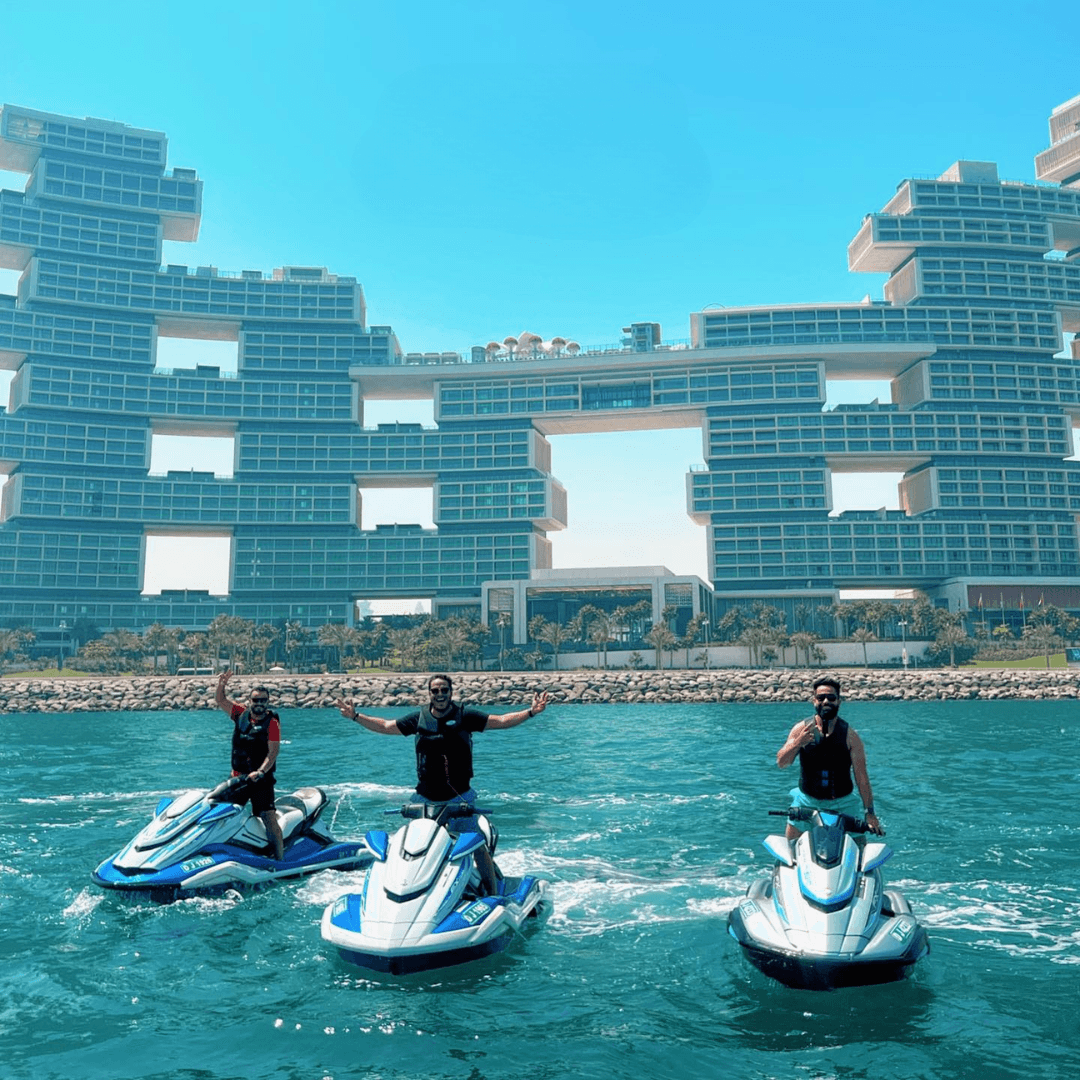 Three jet ski riders posing in front of The Royal Atlantis on Palm Jumeirah during a Ride in Dubai jet ski tour, with the hotel’s unique architecture