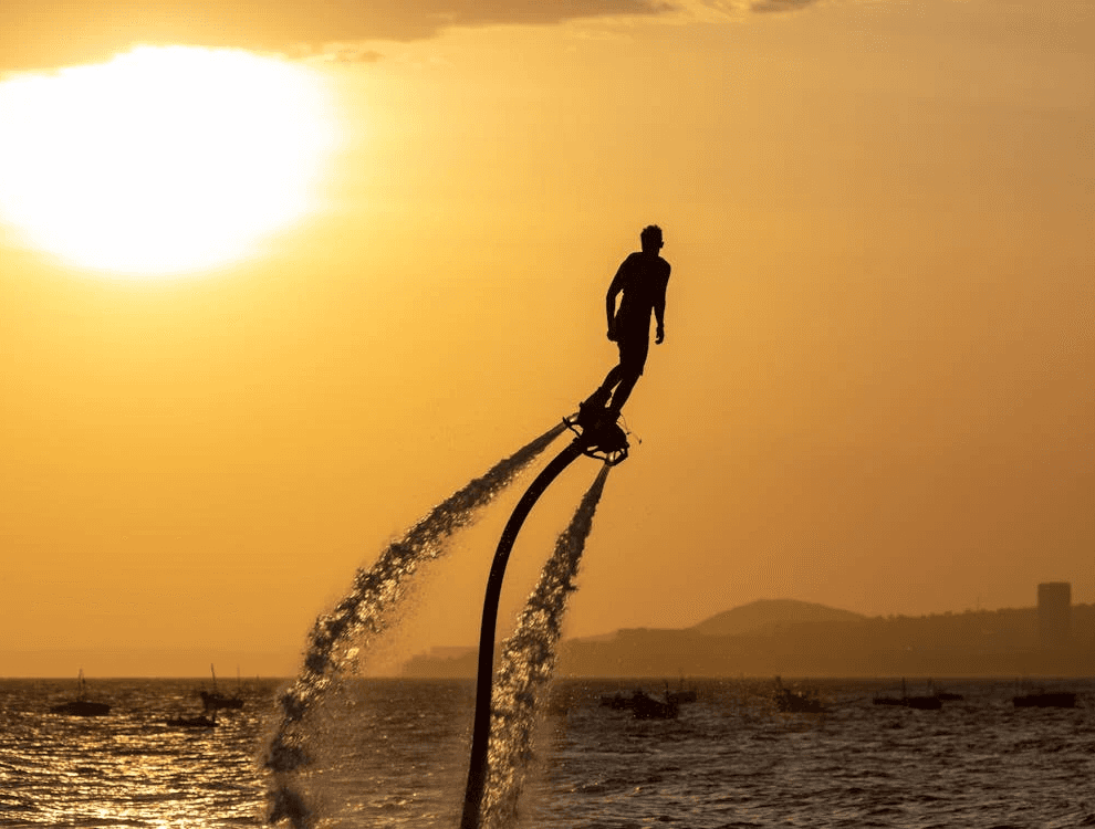 Person flyboarding above the water at sunset in Dubai, enjoying a thrilling birthday experience.