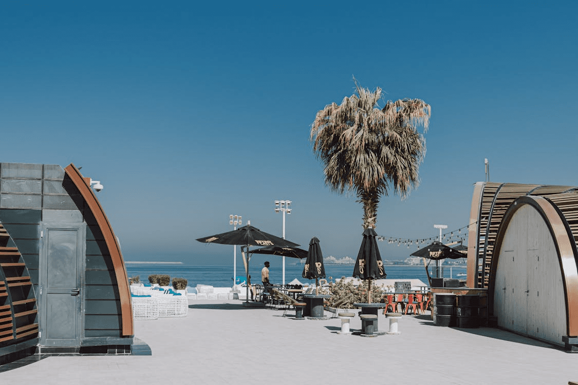 Outdoor seaside dining area with palm tree and shaded tables in Dubai.