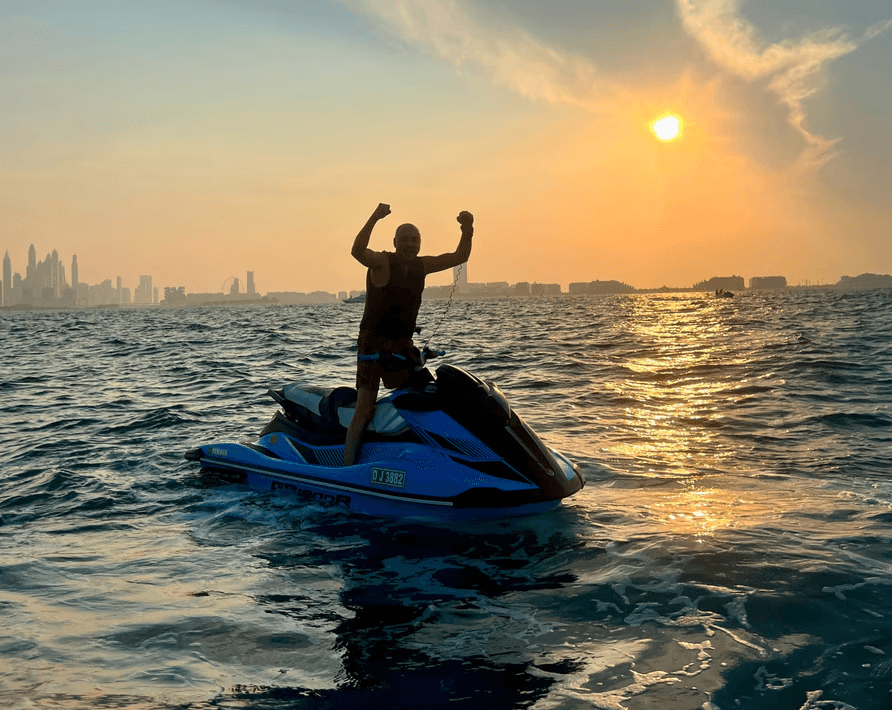 Man celebrating on a jet ski during sunset with Dubai skyline in the background, part of Ride in Dubai’s jet ski experience for water activities in Dubai