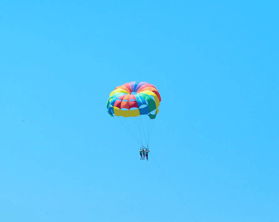 Two people parasailing under a colorful parachute high above the sea in Dubai