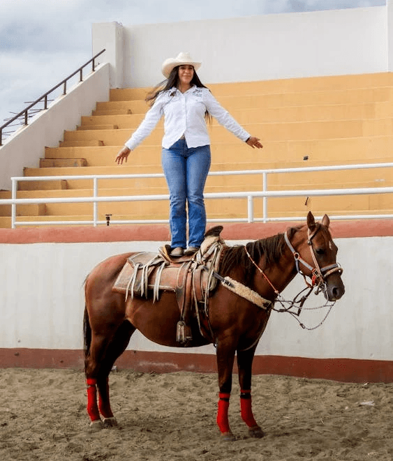 Woman standing on a horse at a stable, taking part in a horseback riding session for a unique birthday activity in Dubai.
