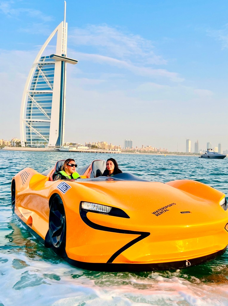 Two women riding an orange jet car on the water near Burj Al Arab in Dubai, enjoying skyline views and a unique water adventure.