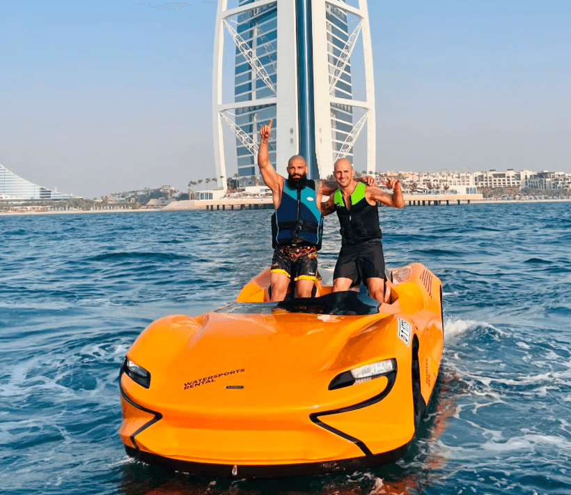 Two men riding a bright orange jet car in front of Burj Al Arab during Ride in Dubai’s premium water activities in Dubai experience