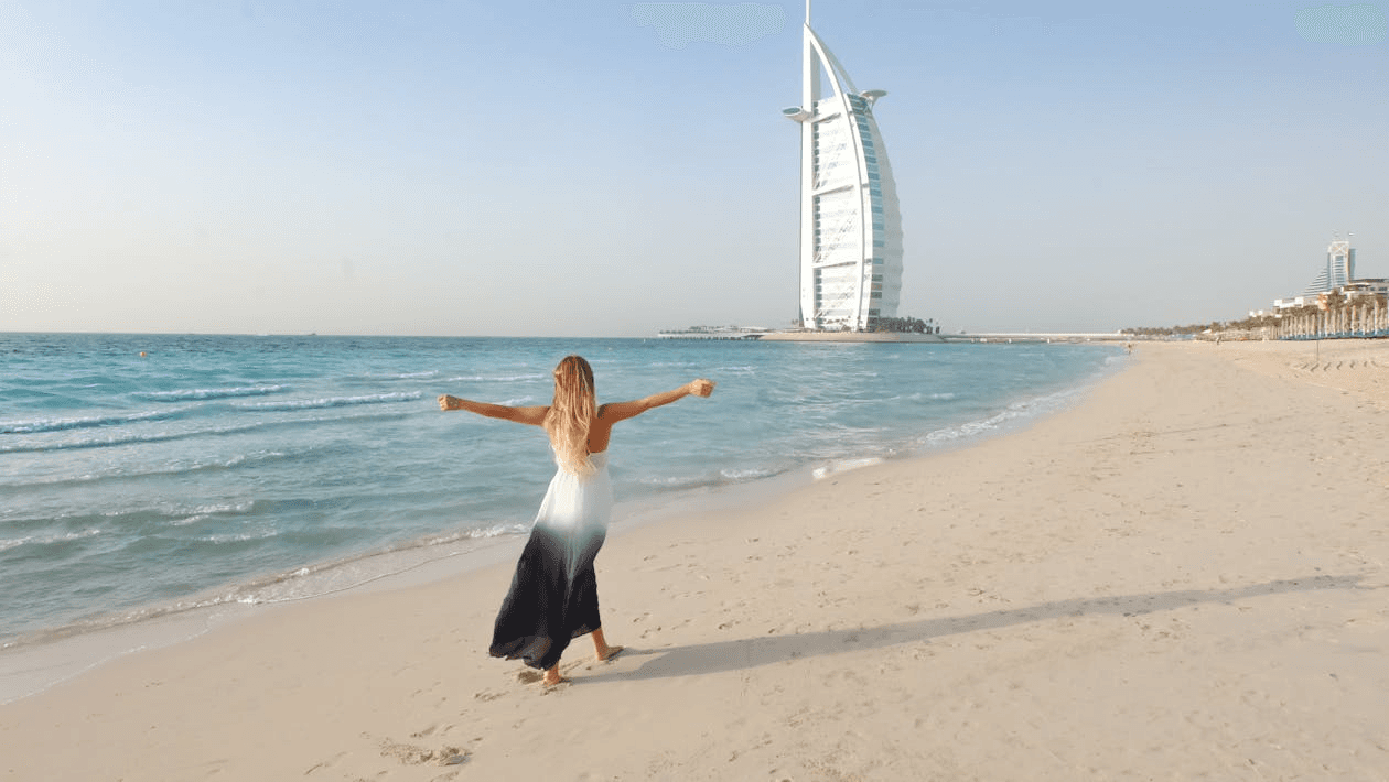 A woman walking along the beach with Burj Al Arab in the background, a peaceful family-friendly beach in Dubai.