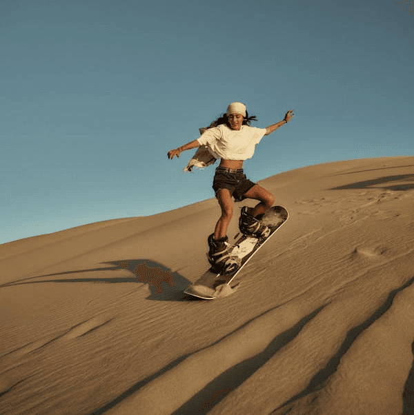 Woman sandboarding down a desert dune, enjoying an adventurous birthday in Dubai’s desert landscape.