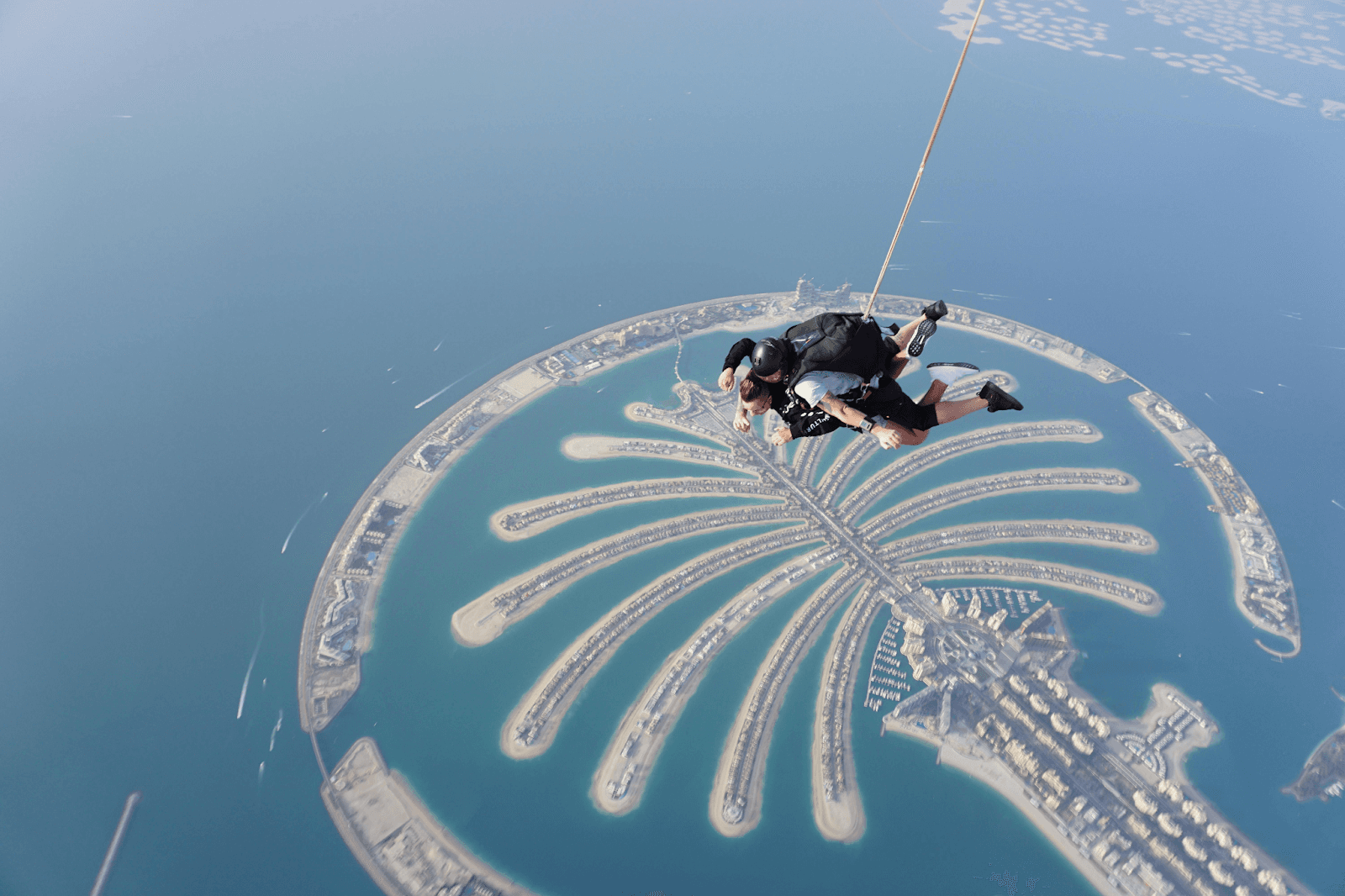 Two people skydiving over Palm Jumeirah on a clear summer day.