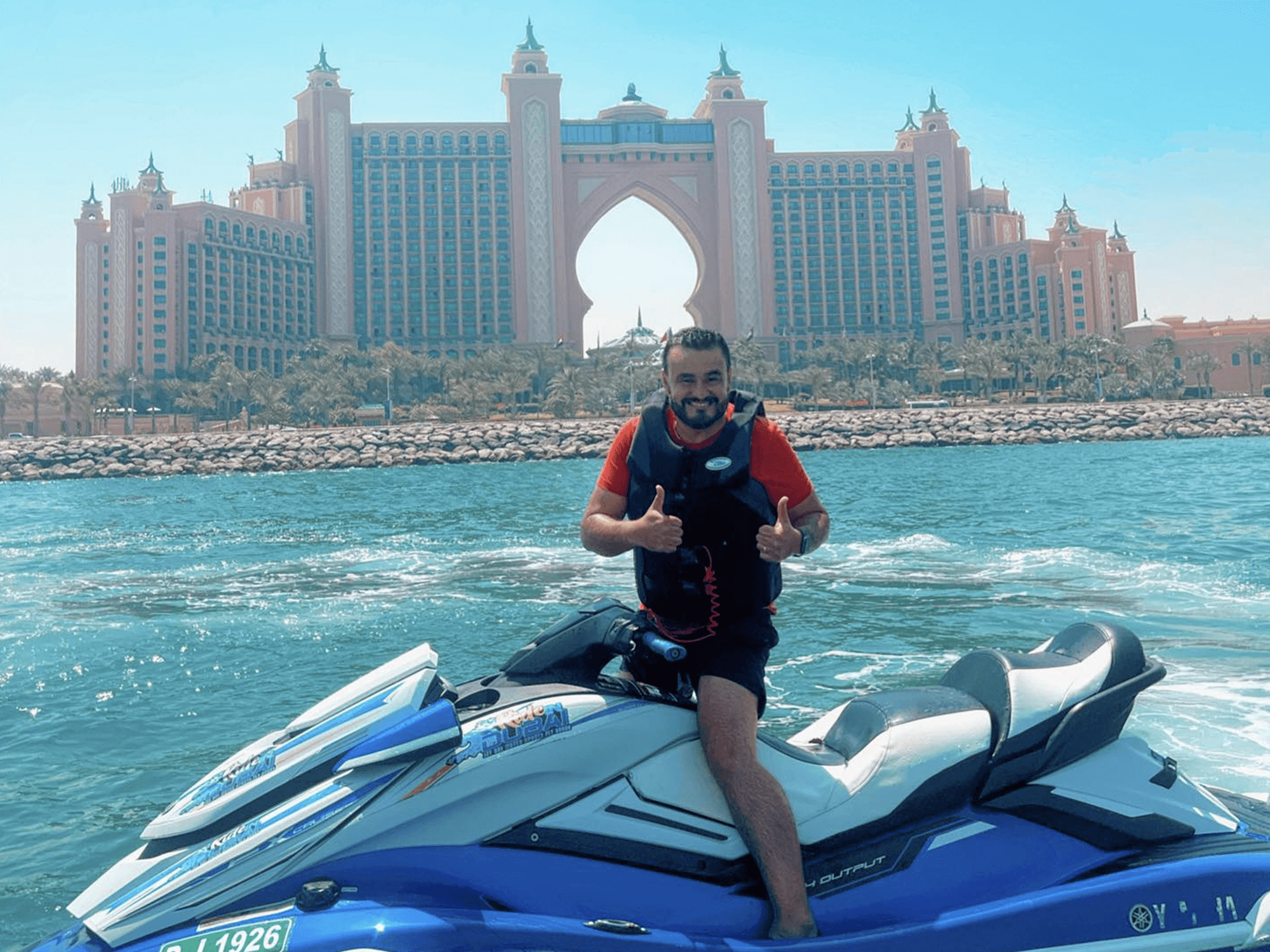Jet ski rider reaching out towards the water with luxury resorts of Palm Jumeirah in the background