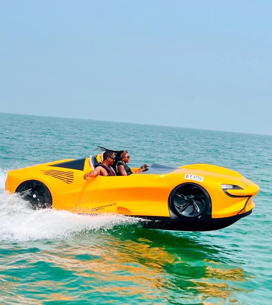 A couple riding an orange jet car on the Arabian Gulf during a thrilling jet car experience in Dubai with water splashes.