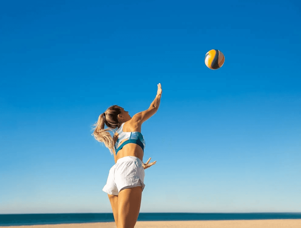 Woman playing beach volleyball under a clear blue sky, celebrating a fun and active birthday at the beach in Dubai.