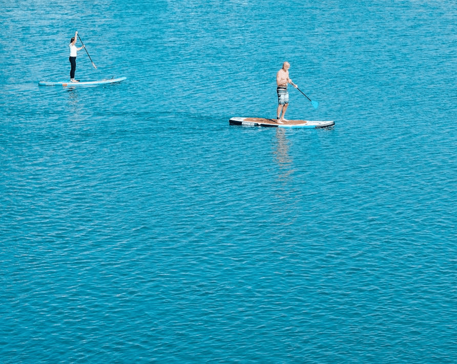 Two people stand-up paddleboarding on calm blue water in Dubai during a watersports session