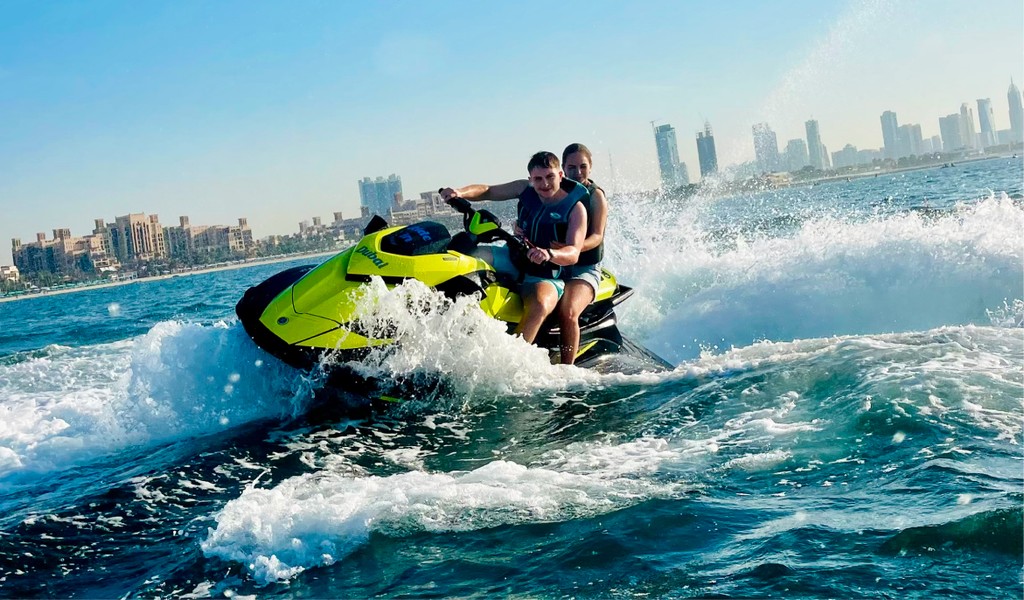 A couple riding a jet ski on the Arabian Gulf with skyline views, part of the jet car and jet ski adventure experiences in Dubai.